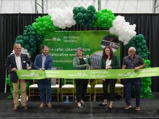Air Products representatives standing across a stage under a green and white balloon arch holding a long ribbon reading Air Products Membrane Solutions; one representative is holding large pair of scissors, preparing to cut ribbon